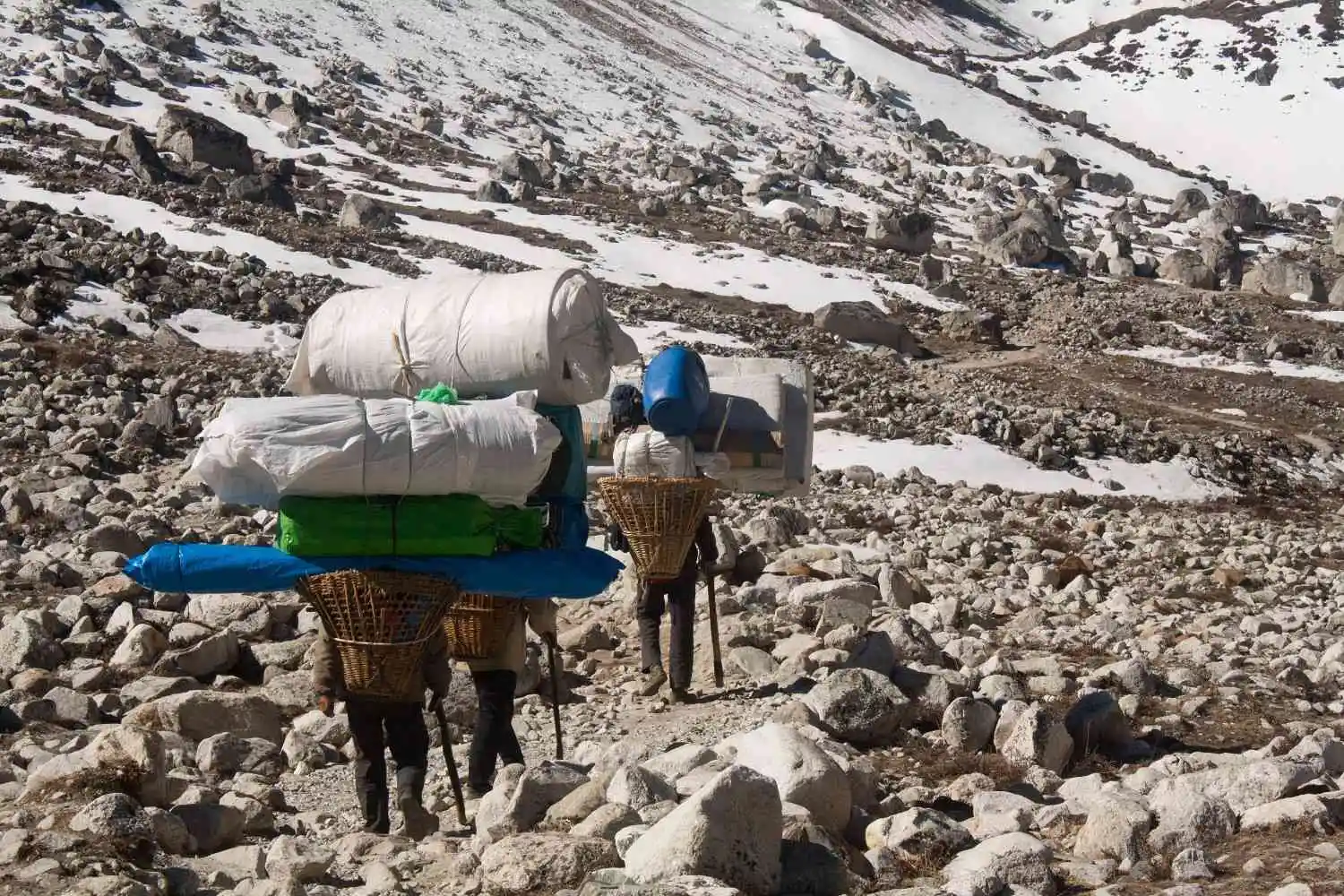 An Everest porter carrying a heavy load in a bamboo doko basket, navigating a steep, rocky trail on the way to Everest Base Camp.