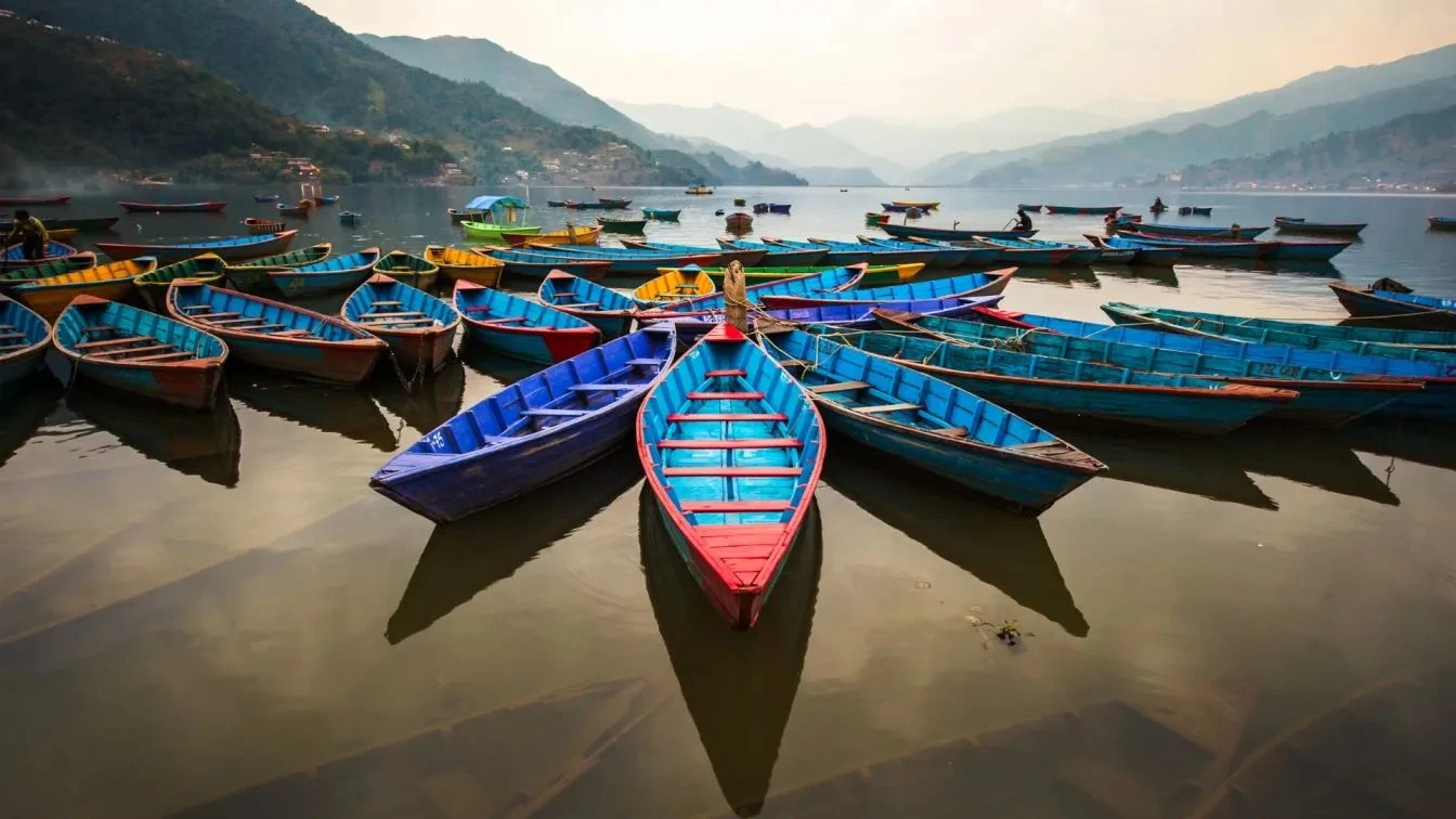 Colorful wooden boats on Phewa Lake surrounded by hills in Pokhara, Nepal