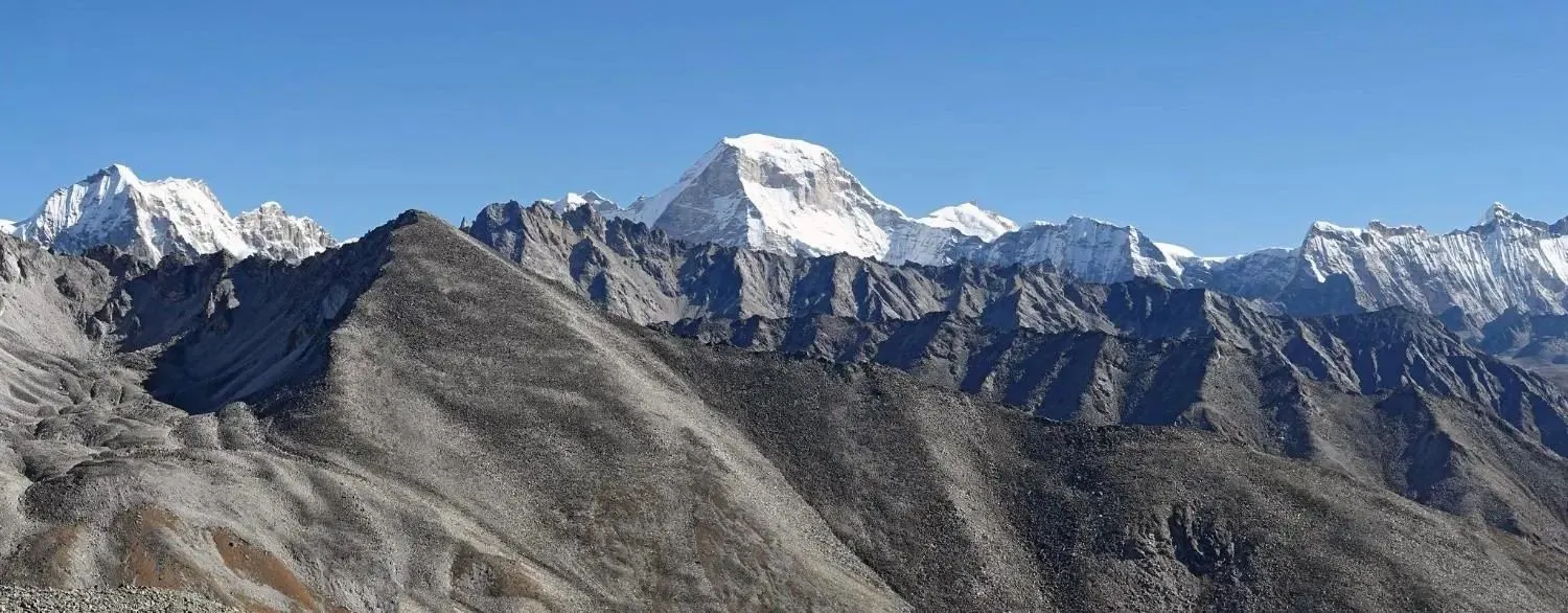 Panoramic view of snow-capped Himalayan mountains and rugged peaks under a clear blue sky in Nepal