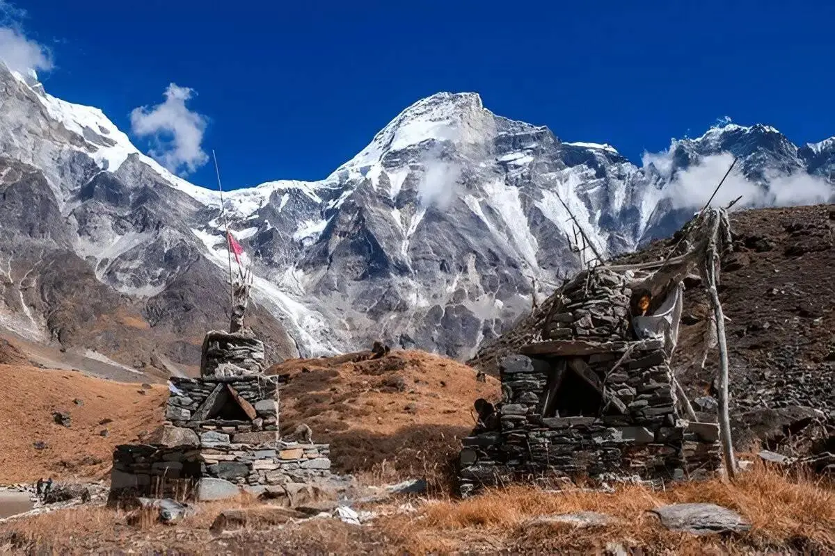 Snow-covered Himalayan peaks rising above a rugged mountain landscape with traditional stone structures in Nepal
