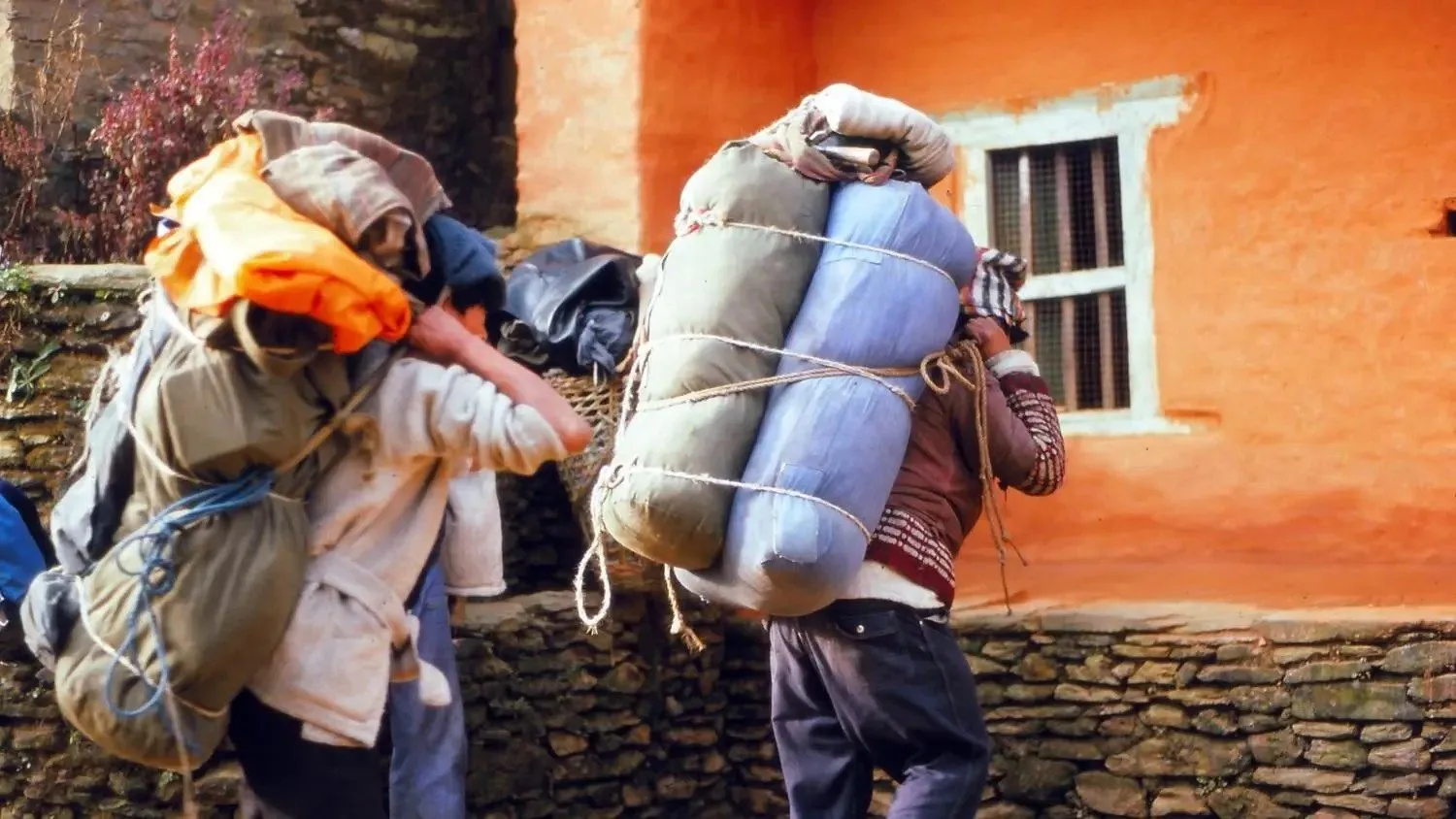 Porters carrying heavy loads with ropes and baskets near a mountain village in Nepal