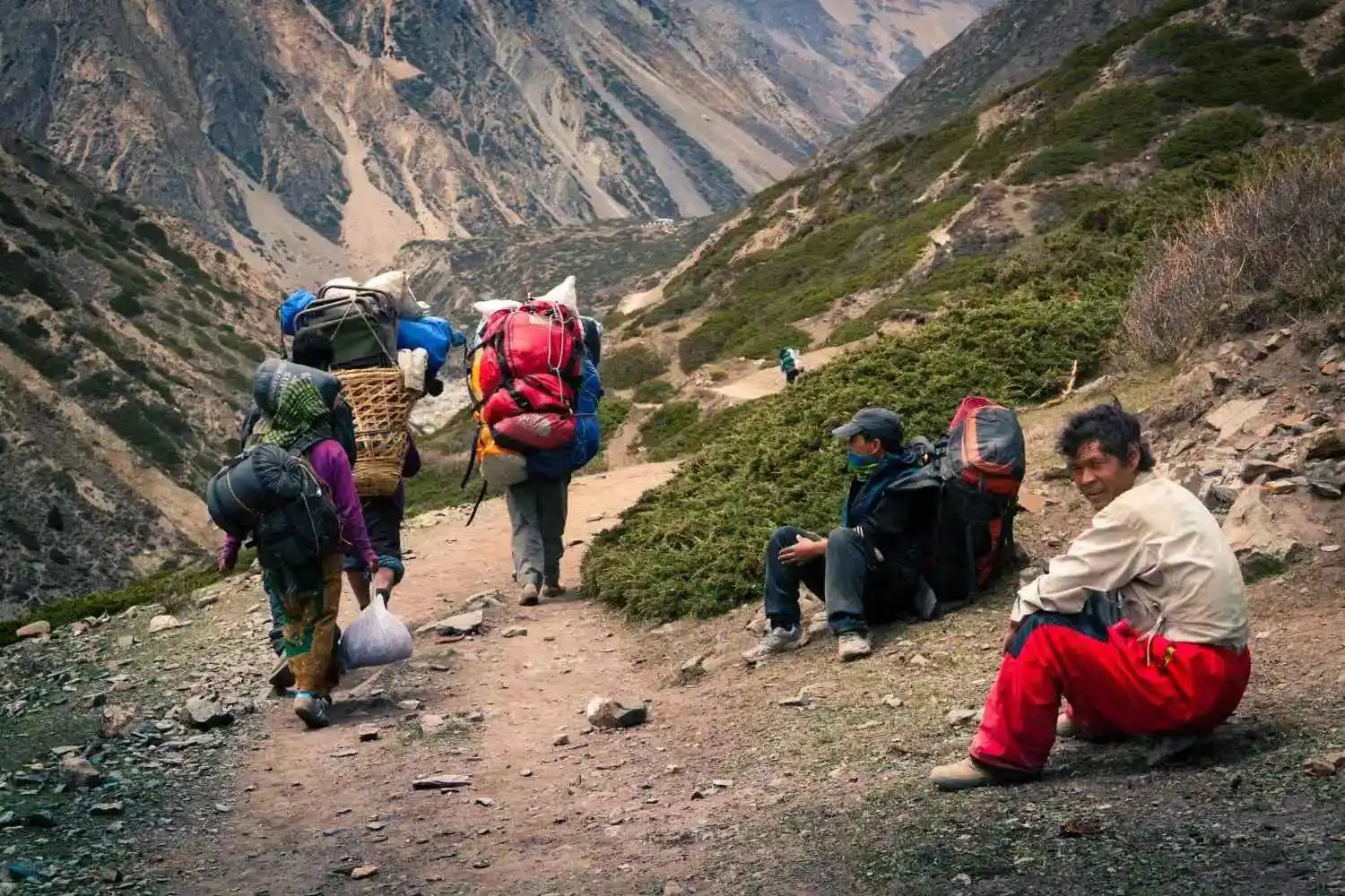Trekking porters carrying large backpacks and supplies along a mountain trail in Nepal