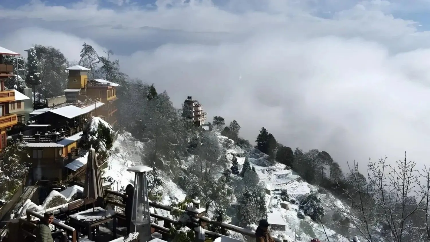 Snow-covered hillside in Nepal with mountain lodges, trees, and winter scenery