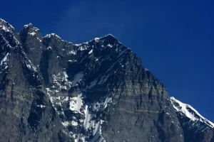 Lhotse Shar mountain with its steep rocky face and snow-covered upper slopes under a clear blue sky.