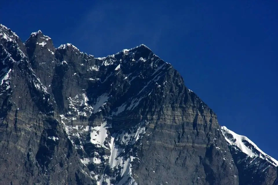 Lhotse Shar mountain with its steep rocky face and snow-covered upper slopes under a clear blue sky.