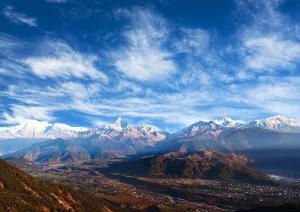 Panoramic view from Panchase Hill showcasing the Annapurna mountain range, Machhapuchhre, green valleys, and a dramatic blue sky with wispy clouds in Nepal.