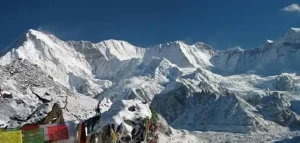 Snow-covered Cho Oyu mountain rising above the Himalayas with colorful prayer flags in the foreground.