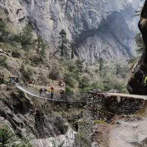 Trekkers crossing a suspension bridge along the Nar Phu Valley Trek beneath towering cliffs in Nepal.