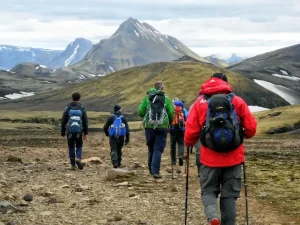 Trekkers hiking along a rocky mountain trail with snow-capped peaks in the background